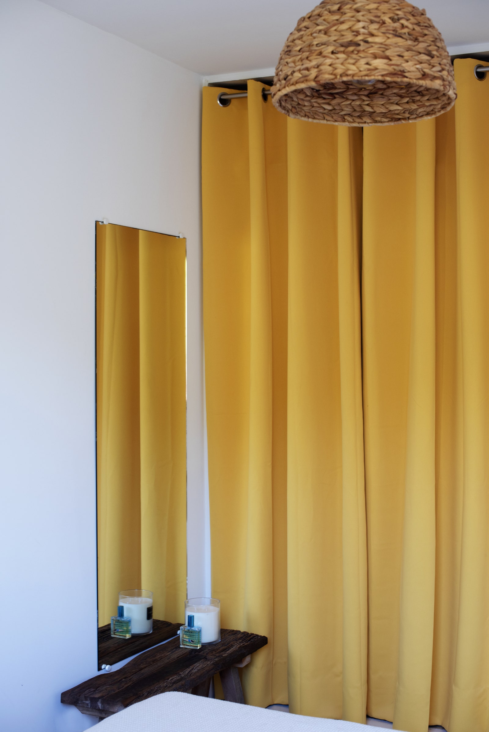 In the bedroom, raw simplicity is awakened by large yellow curtains and a woven straw pendant light.