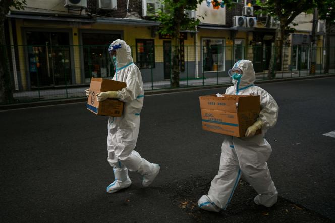 Health workers wearing protective clothing walk on a street next to a residential area under lockdown in Shanghai's Xuhui District on June 8, 2022. 