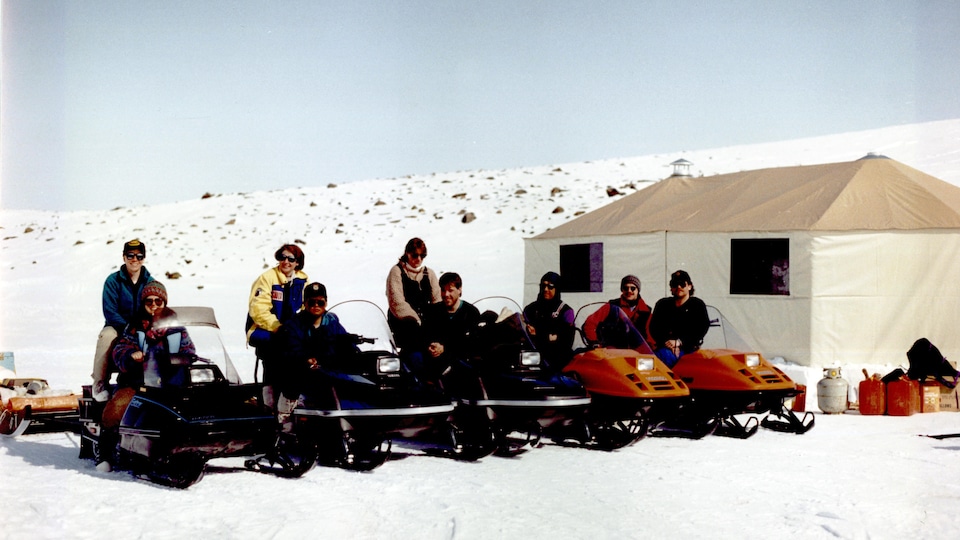 Nine people sitting behind their snowmobile in the spring of 1993.
